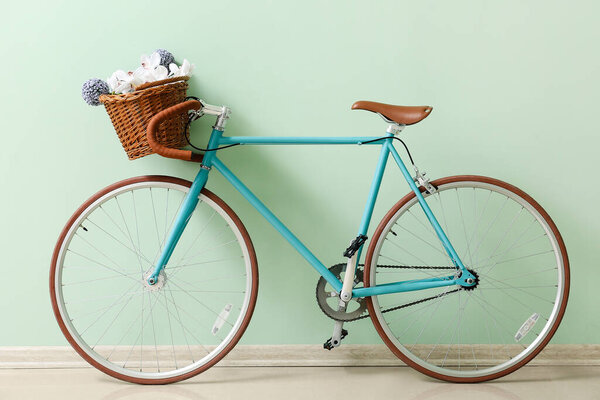 Stylish bicycle with wicker basket and flowers near green wall