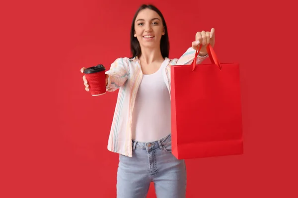 Junge Frau Mit Tasse Kaffee Und Einkaufstasche Auf Rotem Hintergrund — Stockfoto