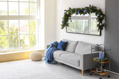 Oturma odasının içinde rahat bir kanepe, büyük bir ayna ve dekore edilmiş köknar ağacı dalı var.