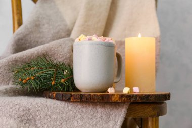 Bir fincan marşmelovlu kakao, köknar dalları, mum ve ekose ışıklı duvarın yanındaki sandalyede. Kış konsepti