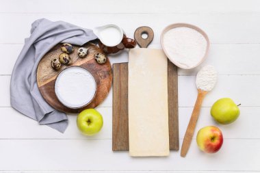 Taze hamur ve elmalı turta malzemeleriyle beyaz ahşap arka planda.