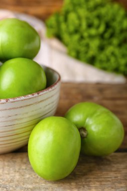 Ahşap arka planda taze yeşil domates kasesi, yakın plan.