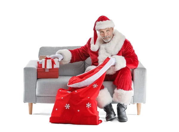 Święty Mikołaj Siedzi Kanapie Wkłada Prezenty Świąteczne Torby Białym Tle — Zdjęcie stockowe