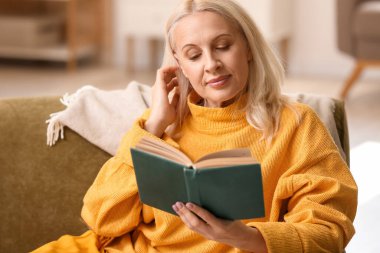 Güz günü evde kitap okuyan güzel olgun bir kadın.