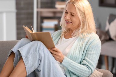 Güz günü evde kitap okuyan güzel olgun bir kadın.