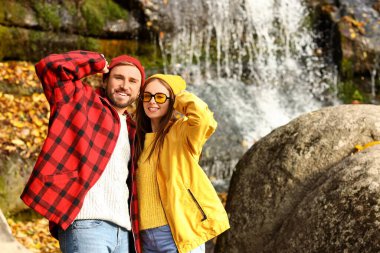 Güneşli bir sonbahar gününde şelalenin yanında güzel genç bir çift.