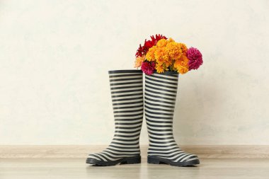 Kauçuk botlar Sonbahar çiçekleriyle aydınlık duvarda