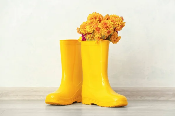 Pair of yellow rubber boots and chrysanthemum flowers against light wall