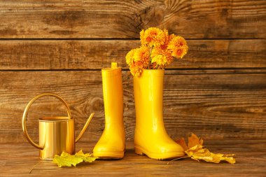 Bir çift sarı lastik bot, sulama kutusu ve ahşap arka planda çiçekler.