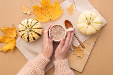 Bej ahşap arka planda bir fincan lezzetli balkabağı kahvesi tutan kadın.