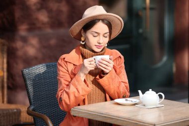 Bir fincan çayla güzel bir kadın sokak kafesinde güneşli bir sonbahar gününün tadını çıkarıyor.