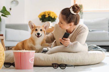 TV uzaktan kumandalı ve evdeki sevimli Corgi köpeği olan genç bir kadın.