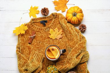 Şık bir süveter, bir fincan çay ve hafif ahşap arka planda sonbahar dekoru.