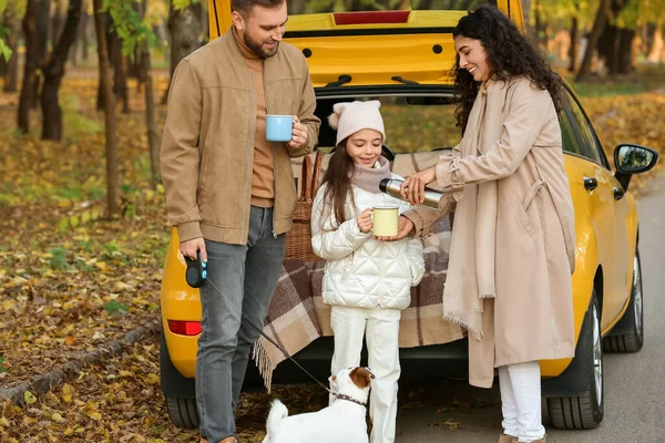 秋の日に黄色い車の近くでかわいい犬が熱いお茶を飲む幸せな家族 — ストック写真