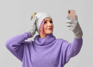 Kışın giyinmiş bir kadın gri arka planda selfie çekiyor.