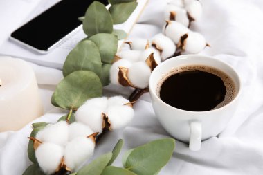 Kumaş yüzeyinde bir fincan kahve, pamuk ve okaliptüs dalları