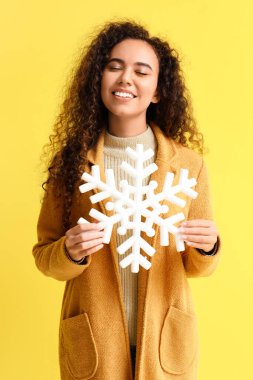 Sarı arka planda büyük kar taneleri olan güzel bir Afro-Amerikalı kadın.