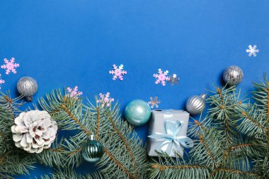 Hediye kutusu, toplar ve mavi arka planda köknar dallarıyla Noel kompozisyonu