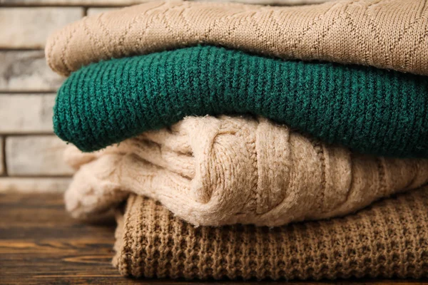 Stack Different Knitted Sweaters Wooden Table Brick Wall Background Closeup — Stock Photo, Image