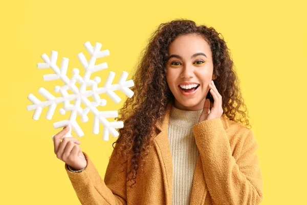黄色の背景に大きな雪の結晶を持つ若いアフリカ系アメリカ人女性を驚かせた — ストック写真