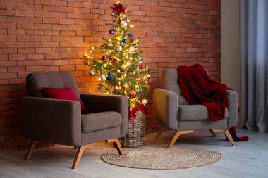 Parlayan ışıkları ve tuğla duvarın yanındaki koltukları olan güzel Noel ağacı.
