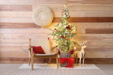 Parlayan ışıkları, koltuğu ve ahşap duvarın yanında ren geyiği olan Noel ağacı.