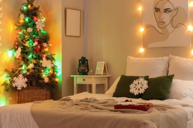 Modern yatak odasının içinde Noel ağacı ve parlayan ışıklar var.
