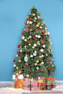 Güzel dekore edilmiş Noel ağacı ve mavi duvarın yanında hediye kutuları