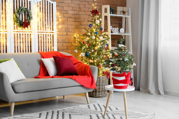 Interior of stylish living room with sofa, Christmas trees and glowing lights
