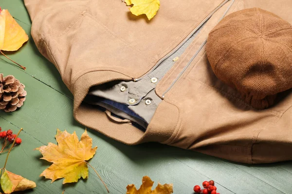 Stylish jacket, shirt, hat and autumn leaves on color wooden table, closeup