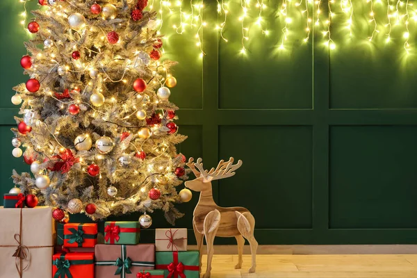美丽的圣诞树 绿墙附近有闪亮的灯光 礼物和木制驯鹿 — 图库照片