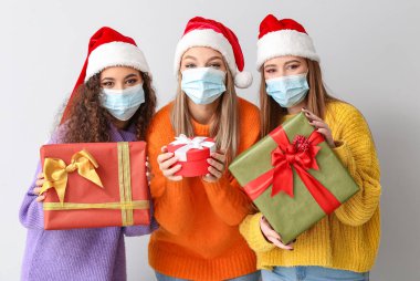 Tıbbi maskeli güzel genç kadınlar ve hafif arka planda Noel hediyeleri.