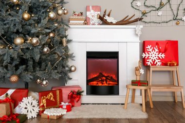 Güzel dekore edilmiş Noel ağacı. Salonda şöminenin yanında hediye kutuları var.