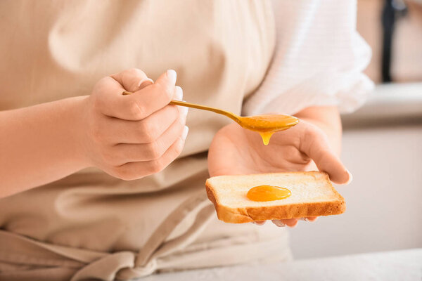 Woman spreading tasty tangerine jam onto toast at table in kitchen, closeup