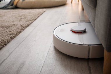 Odadaki kanepenin yanındaki modern robot elektrikli süpürge.