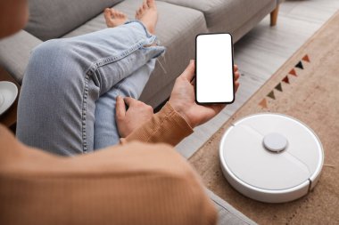 Modern robot elektrik süpürgesinin yanında cep telefonu olan bir kadın.