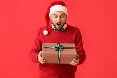 Renkli arka planda Noel hediyesi olan şaşırmış genç bir adam.