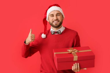Mutlu genç adam, Noel hediyesiyle arka planda baş parmak işareti yapıyor.
