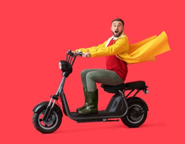 Renkli arka planda bisiklet süren yağmurluk giyen genç adam şaşırdı.