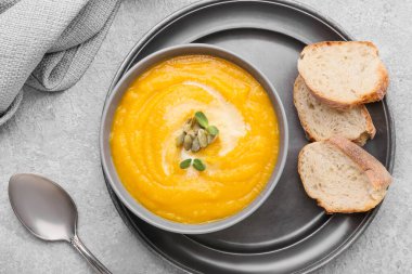 Bir kase lezzetli balkabağı kremalı çorba ve gri arka planda ekmek.