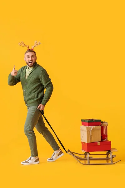 Glücklicher Junger Mann Mit Weihnachtsgeschenken Auf Schlitten Vor Farbigem Hintergrund — Stockfoto