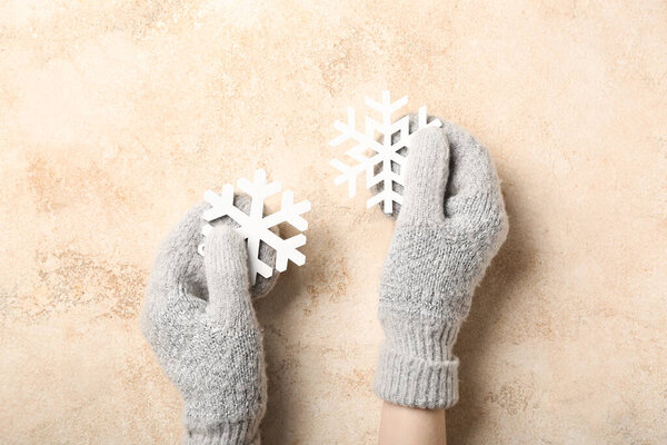 Женщина в теплых перчатках держит снежинки на бежевом фоне