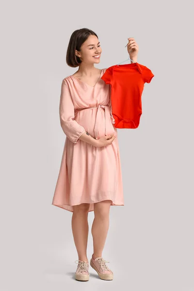 若いです妊娠中の女性とともに赤ちゃんボディスーツ上の光背景 — ストック写真