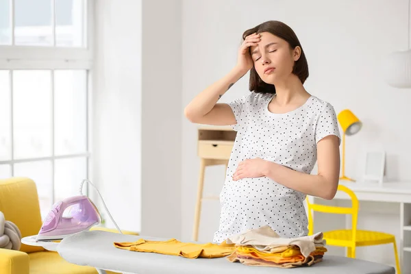 年轻的孕妇厌倦了在家里熨烫婴儿衣服 — 图库照片