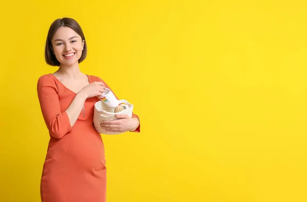 Jovem Grávida Segurando Cesta Com Roupas Bebê Fundo Amarelo — Fotografia de Stock