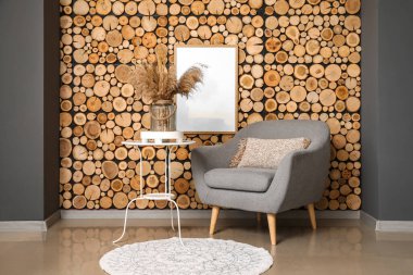 Masada kuru kamışlı cam vazo ve tahta duvarın yanında gri koltuk.