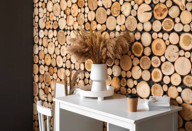 Vazoda kuru sazlıklar ve ahşap duvarın yanında bir fincan kahve olan modern işyeri.