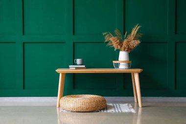 Kuru sazlıklar, fincanlar ve yeşil duvarın yanındaki bankta duran kitaplar.