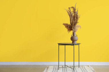 Sarı duvarın yanındaki masada otlu vazo ve sazlık ayırıcı.