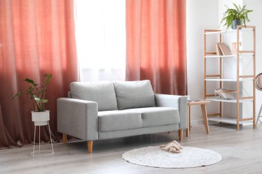 Gri kanepe, raf ünitesi ve kırmızı perdelerle aydınlık oturma odasının içinde.